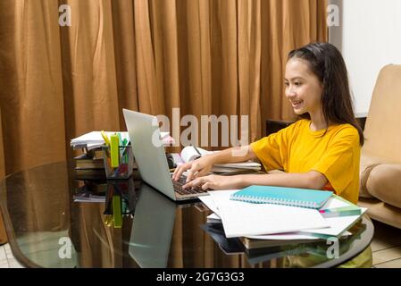 Bambina asiatica che fa il suo lavoro con il laptop a casa. Formazione online durante la quarantena Foto Stock