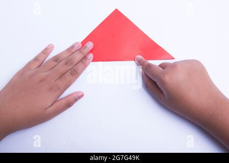 Mano umana che piega una carta colorata isolata su sfondo bianco Foto Stock