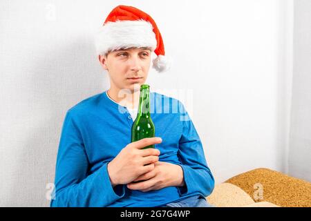 Giovane uomo a Santa Hat con una bottiglia di birra presso il muro in camera Foto Stock