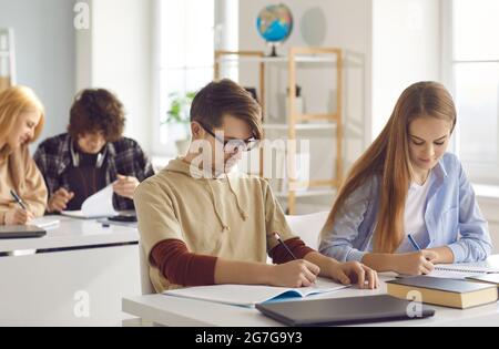 Gli studenti adolescenti concentrati scrivono l'esame di gruppo che si sottopone a test in classe Foto Stock