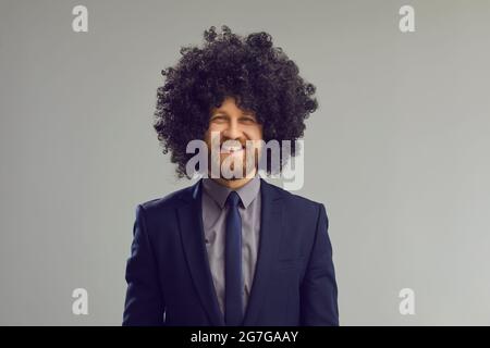 Studio ritratto di felice sorridente giovane uomo d'affari in un vestito e divertente parrucca riccia Foto Stock