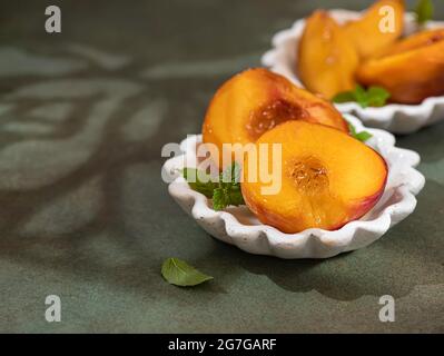 Pesche caramellate al miele, con foglie di menta su fondo di cemento con ombre. Dessert estivo. Spazio di copia Foto Stock