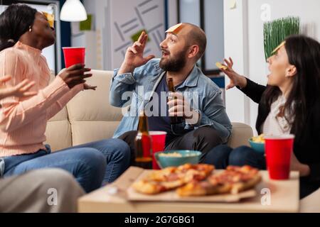 Una squadra diversificata di colleghi che giocano a incantati dopo il lavoro in ufficio. Gli amici multietnici si divertono a indovinare il gioco d'imiation come divertenti e allegri intrattenimenti con cibo e bevande Foto Stock