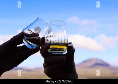 Bere whisky alla distilleria Ardnahoe sull'isola di Islay della costa occidentale della Scozia con i Paps del Giura all'orizzonte. Foto Stock