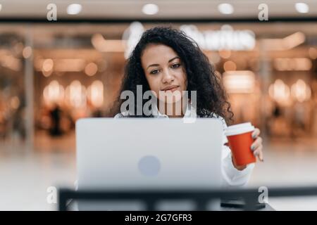primo piano. la giovane donna con un caffè da asporto sta lavorando sul suo laptop. Foto Stock