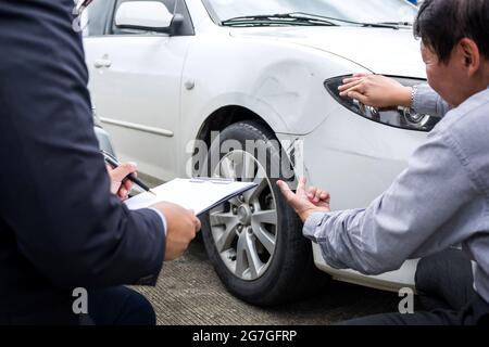 Uomo agente riempire modulo di assicurazione vicino danneggiato ed esaminare automobile, incidente stradale e concetto di assicurazione. Foto Stock