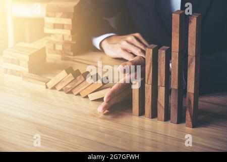 Primo piano di uomo d'affari mano arresto caduta Dominoes effetto di legno da continuo rovesciato o rischio, strategia e concetto di intervento di successo per Foto Stock