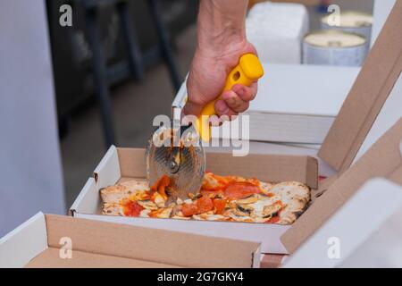 Uomo mani taglio pepperoni pizza con salame e funghi - primo piano Foto Stock