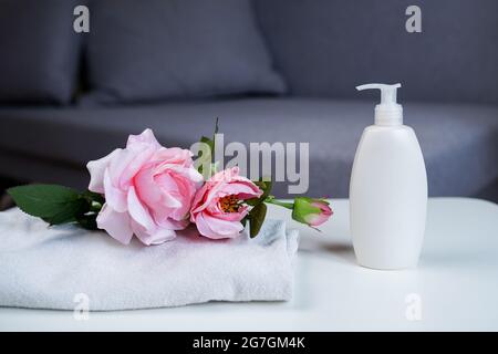 prodotto per la cura del corpo bottiglia bianca con gel doccia o shampoo e asciugamano con rosa fiori. Preparazione del bagno. Interno della stanza. Foto Stock