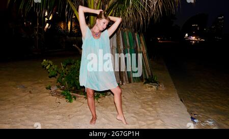 Donna caucasica europea orientale mezza età capelli biondi pelle chiara pallida carnagione in See Thru Dress di notte posando sulla sabbia indossando un collo senza collo Foto Stock