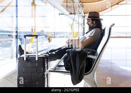 Il ragazzo nel cappello all'aeroporto nella sala d'attesa seduto in attesa del suo volo Foto Stock