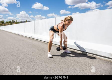 Giovane Donna allenarsi con il suo manubrio all'aperto, vista laterale Foto Stock