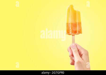 Donna tiene il gelato morso su sfondo giallo con spazio di copia. Colore popsicle di frutta surgelata. Foto Stock