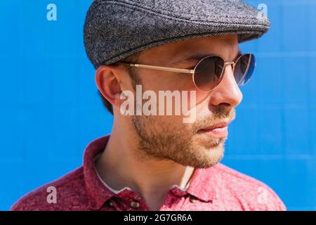 Giovane ragazzo con il bearded che indossa una polo casual rossa e un cappuccio in piedi contro il muro blu sulla strada nel giorno d'estate Foto Stock