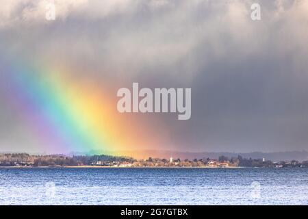L'arcobaleno spotty illumina la piccola città sulla riva del mare, fronte tuoso sullo sfondo, Germania, Baviera, lago Chiemsee, Seebruck Foto Stock