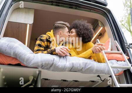 Vista laterale di diversi uomini e donne baciarsi mentre sdraiati sul letto in un pulmino moderno durante il viaggio Foto Stock