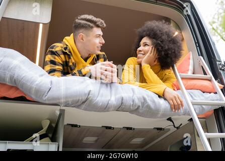 Angolo basso di Afro American Woman sorridente per il giovane ragazzo mentre sdraiato sul letto in furgone durante il viaggio in auto guardando l'un l'altro Foto Stock