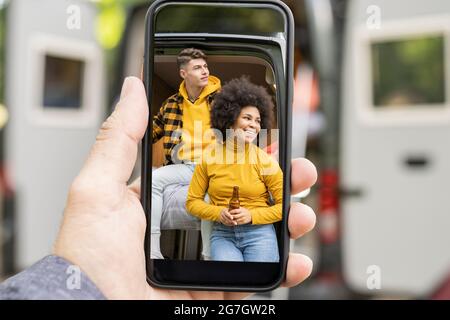 Mano tagliata irriconoscibile che mostra la foto di diverse coppie seduti sul pulmino il giorno del fine settimana in natura guardando via Foto Stock