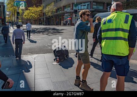 Le persone che si trovano in un incrocio di strada nel centro di Sydney, Australia, ignorano una persona che inginocchiava e tiene una tazza che si inginocchiava in un giorno d'inverno Foto Stock