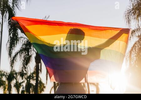 Silhouette di anonimo gay maschile in piedi con bandiera iridata