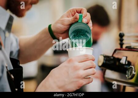 Barista professionista irriconoscibile che prepara da vicino la schiuma di latte caldo, latte di pourin in una tazza di carta con cappuccino al caffè Foto Stock