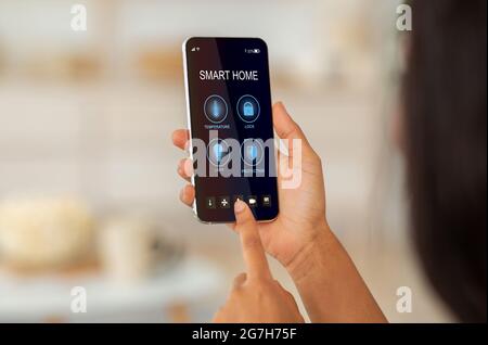 Sistema di controllo remoto della casa sul telefono digitale. Concetto di casa e tecnologia intelligente. Donna multirazziale che gestisce la temperatura, la ventilazione e l'illuminazione su SM Foto Stock