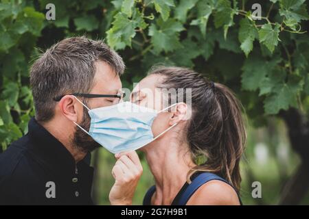 Coppia di amanti che baciano dietro la maschera protettiva - nuovo concetto di stile di vita normale con coppia in amore bacio all'aperto Foto Stock