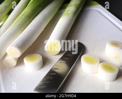 porri su un tagliere con un coltello affilato e alcune parti tagliate Foto Stock