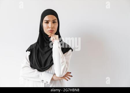 Una donna musulmana sconvolguta in hijab pensando a qualcosa e strinzire la sua fronte mentre si trova nello studio bianco Foto Stock