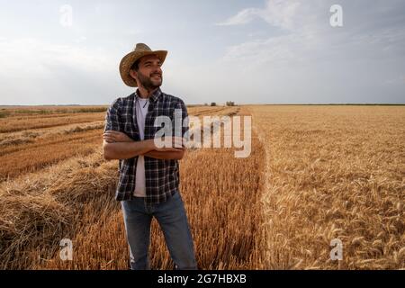 Coltivatore è in piedi davanti al suo campo di grano mentre la raccolta è in corso. Foto Stock