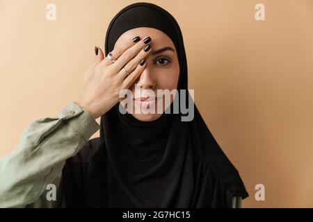 Un ritratto della donna musulmana che ricopre il suo occhio con una mano mentre si trova nello studio arancione Foto Stock