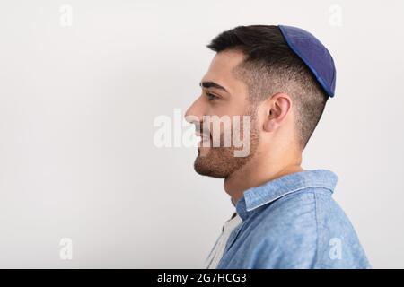 Profilo Vista laterale headshot ritratto di bel ragazzo ebreo sorridente in posa in studio, guardando da parte, indossando kippah, in posa isolato su stu bianco chiaro Foto Stock