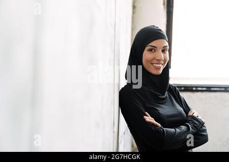 Giovane sportiva musulmana in hijab ridendo mentre si trova in casa Foto Stock