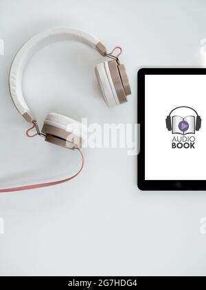 Tablet con icona per audiobook e cuffie su sfondo bianco. Concetto di biblioteca digitale. Scatto in testa. Spazio di copia. Foto Stock