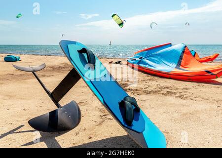 Primo piano aliscafo surf e attrezzatura kite sulla spiaggia di sabbia spiaggia di sport acquatici luogo in giornata di sole luminoso contro mare costa oceanica con molti kiter Foto Stock