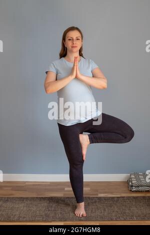 Donna incinta che pratica yoga, in piedi in posa albero o vriksasana Foto Stock