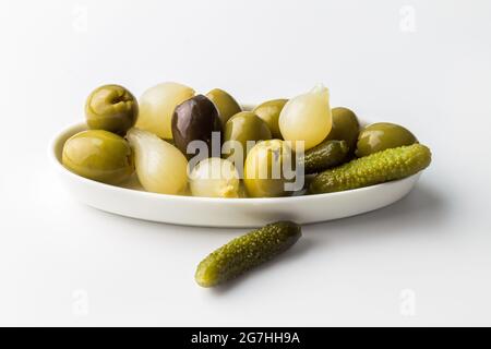 Sottaceti assortiti, cipolle e olive in piastra bianca isolata su sfondo bianco con spazio per la copia Foto Stock