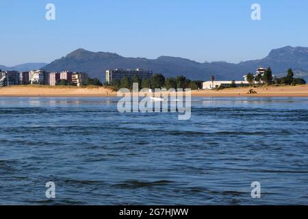 Vista attraverso la baia da Santona verso Laredo e una piccola barca che passa di fronte a escursionisti di prima mattina sulla spiaggia Spagna Foto Stock