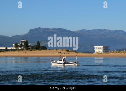 Vista attraverso la baia da Santona verso Laredo e una piccola barca che passa di fronte a escursionisti di prima mattina sulla spiaggia Spagna Foto Stock