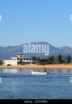 Vista attraverso la baia da Santona verso Laredo con il suo edificio Royal Nautical Club e una piccola barca che passa di fronte a camminatori di prima mattina Spagna Foto Stock