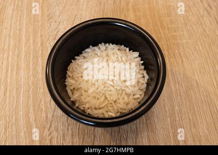 Ciotola nera con riso bianco. Grano di riso crudo. Grano di riso bianco. Foto Stock