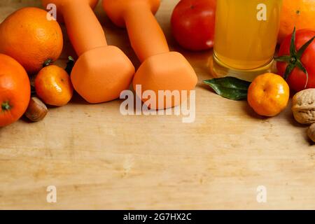 Manubri, succo d'arancia, frutta e noci sul tavolo di legno, concetto di stile di vita sportivo e di salute Foto Stock