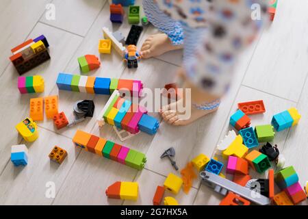 bambino ragazzo che gioca con sua madre in kit di costruzione per bambini a colori. I dettagli del kit di costruzione per bambini sono sparsi sul pavimento. Foto Stock