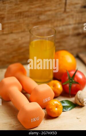 Manubri, succo d'arancia, frutta e noci sul tavolo di legno, concetto di stile di vita sportivo e di salute Foto Stock