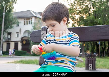 Un bambino di 4 anni gioca con Pop IT nel parco cittadino. Giocattolo antistress per lo sviluppo di belle abilità motorie nei bambini. Foto Stock