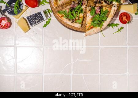 Pizza fatta in casa con funghi, pancetta, rucola e formaggio, su piastrelle estate soleggiato sfondo. Le mani della ragazza in tagli pic e prende una fetta di pizza top vie Foto Stock