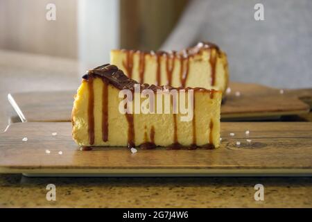 Due pezzi di cheesecake su tavole da servizio in legno sul tavolo nel cafe. Primo piano. Messa a fuoco selettiva. Foto Stock