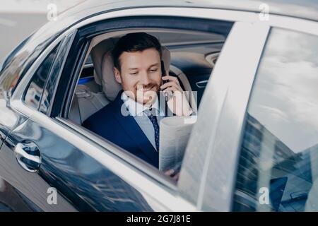 Felice giovane proprietario di affari che legge giornale in auto Foto Stock