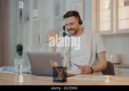 Concetto di e learning. Felice studente uomo bearded ha video conferenza studi online onde palma in laptop display saluta insegnanti lavora usi a distanza Foto Stock