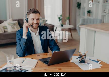 Soddisfatto professionista bearded uomo imprenditore orologi educativo business webinar online indossa cuffie looksat laptop ha lontano lavoro computer Foto Stock